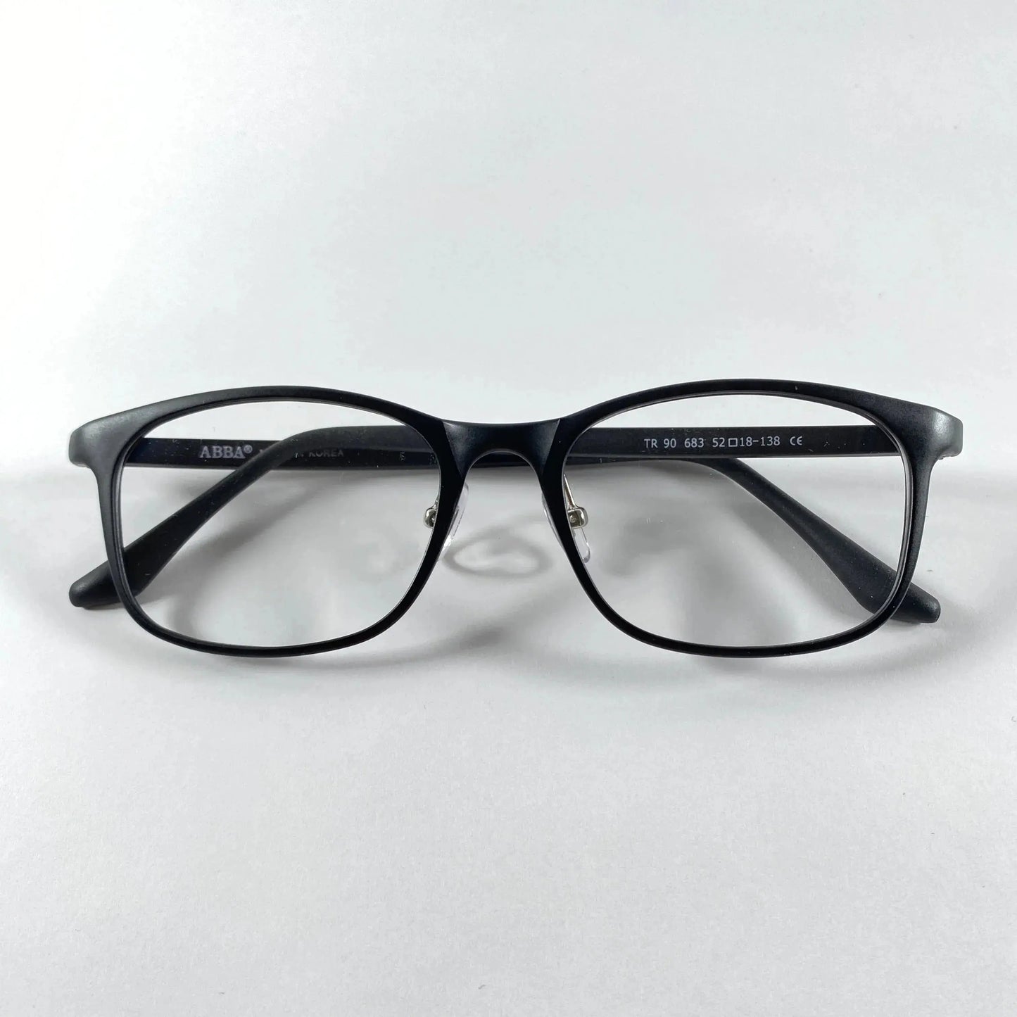 Black square eyeglasses with clear lenses on a white background, ABBA brand detail visible