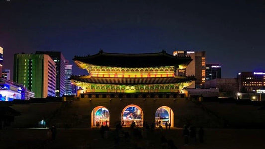 Gwanghwamun Palace Gate glowing gold against Seoul's modern skyline at night