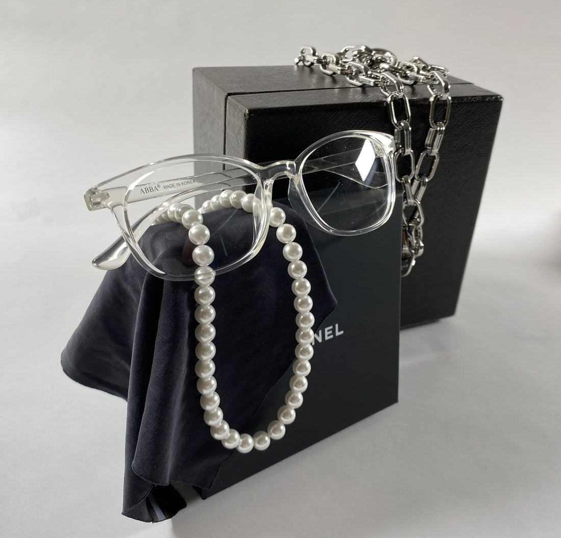 light clear transparent glass frames with square shape are displayed draped with a pearl necklace, set against black boxes.