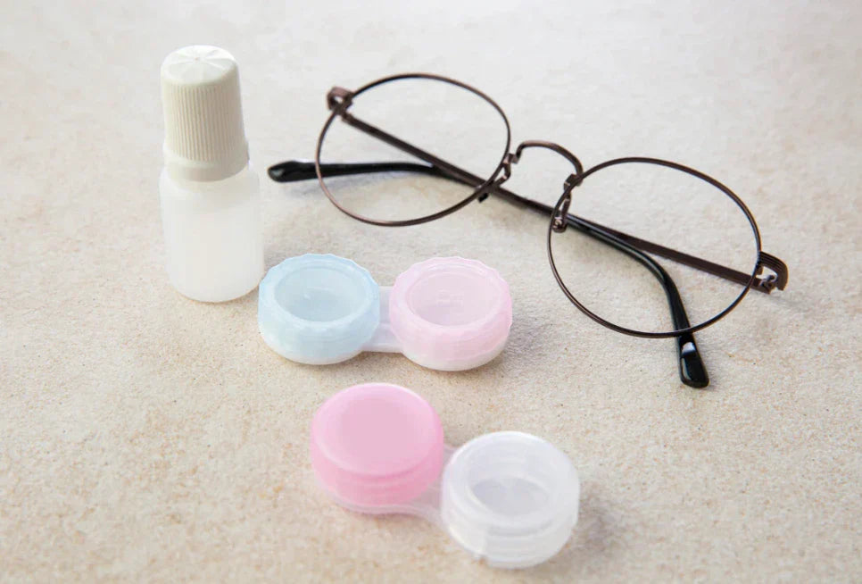 Round eyeglasses next to contact lens cases, contact lens solution, comparing glasses and contact lenses.