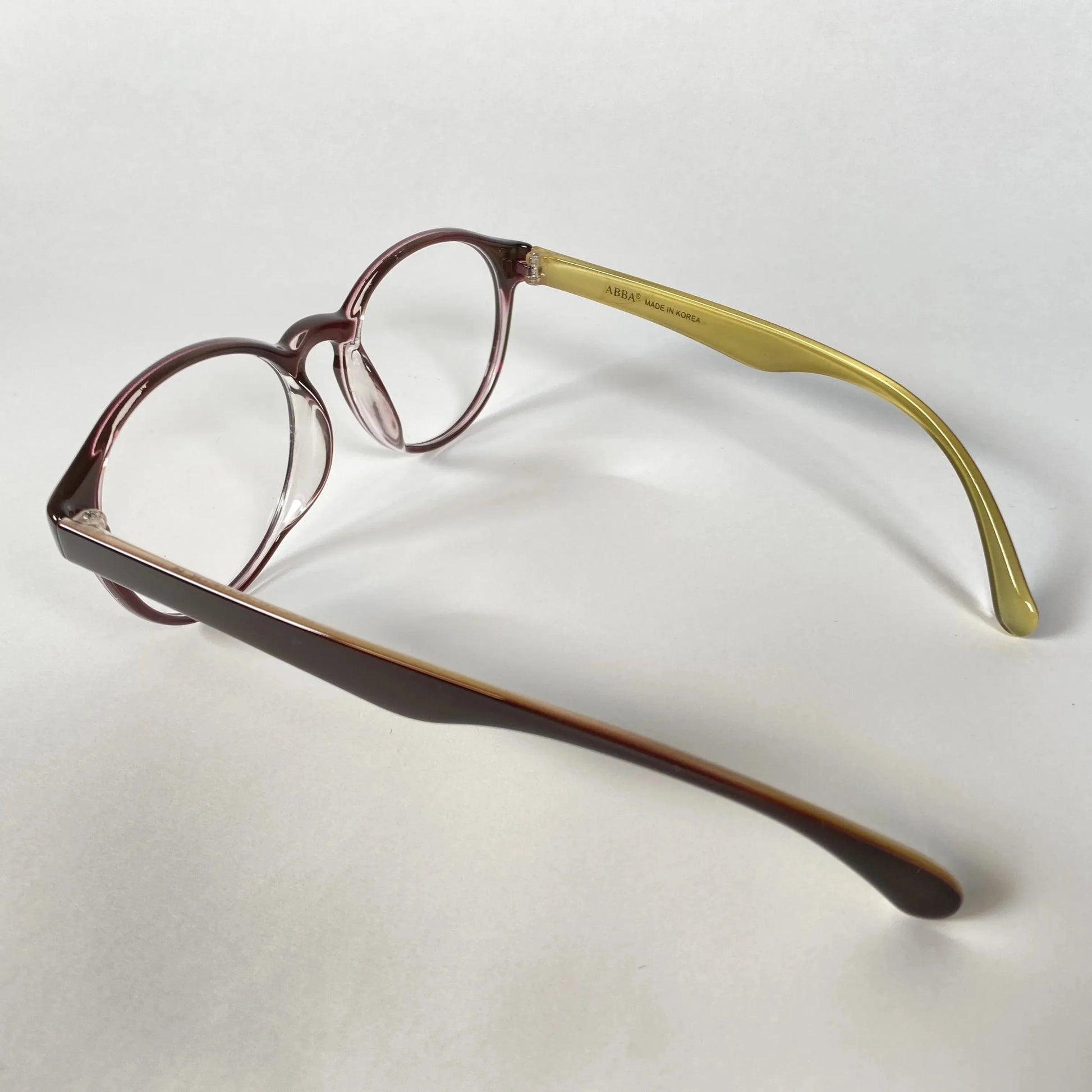Glossy brown round eyeglasses with yellow temples on white background
