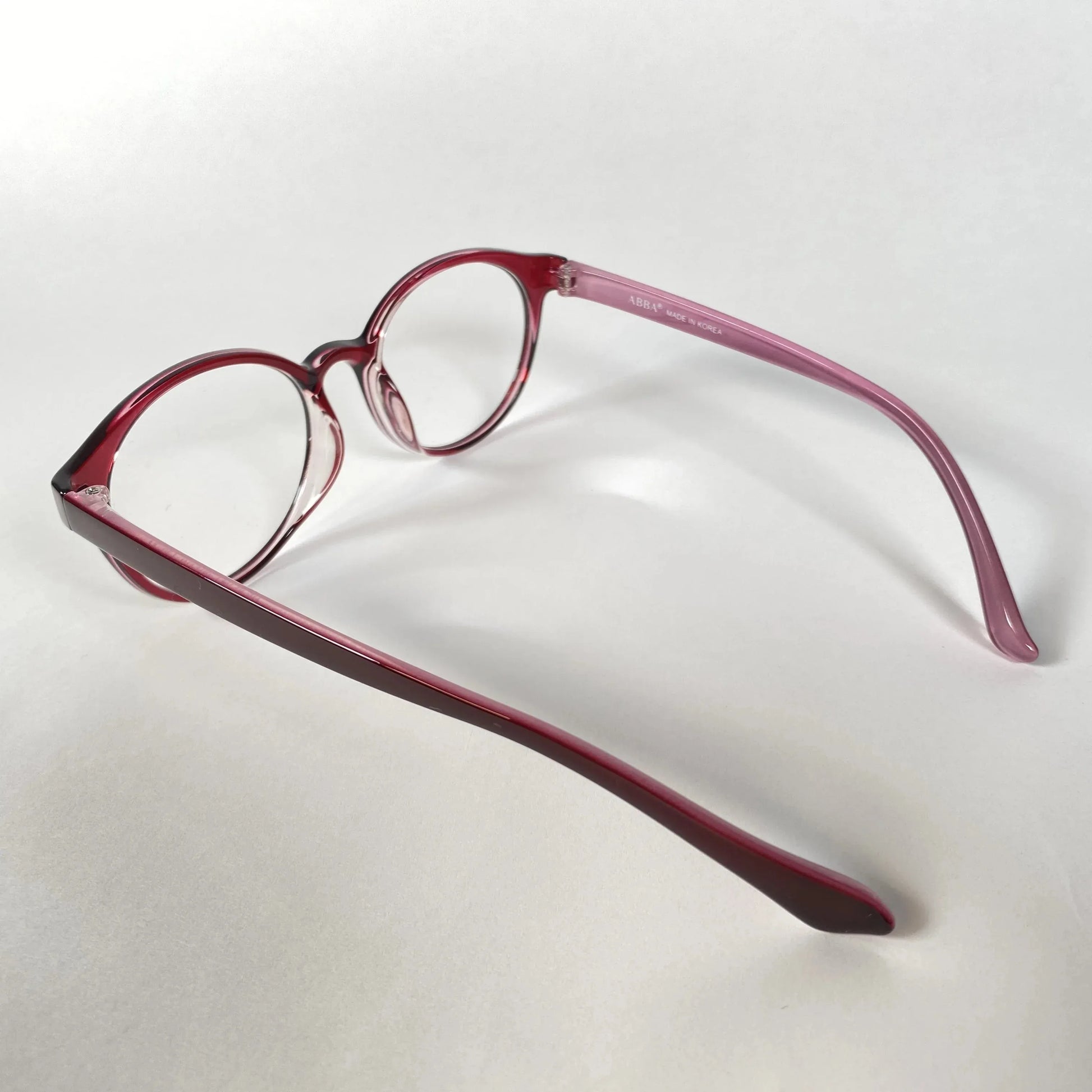 Round burgundy eyeglasses with clear lenses on a white background