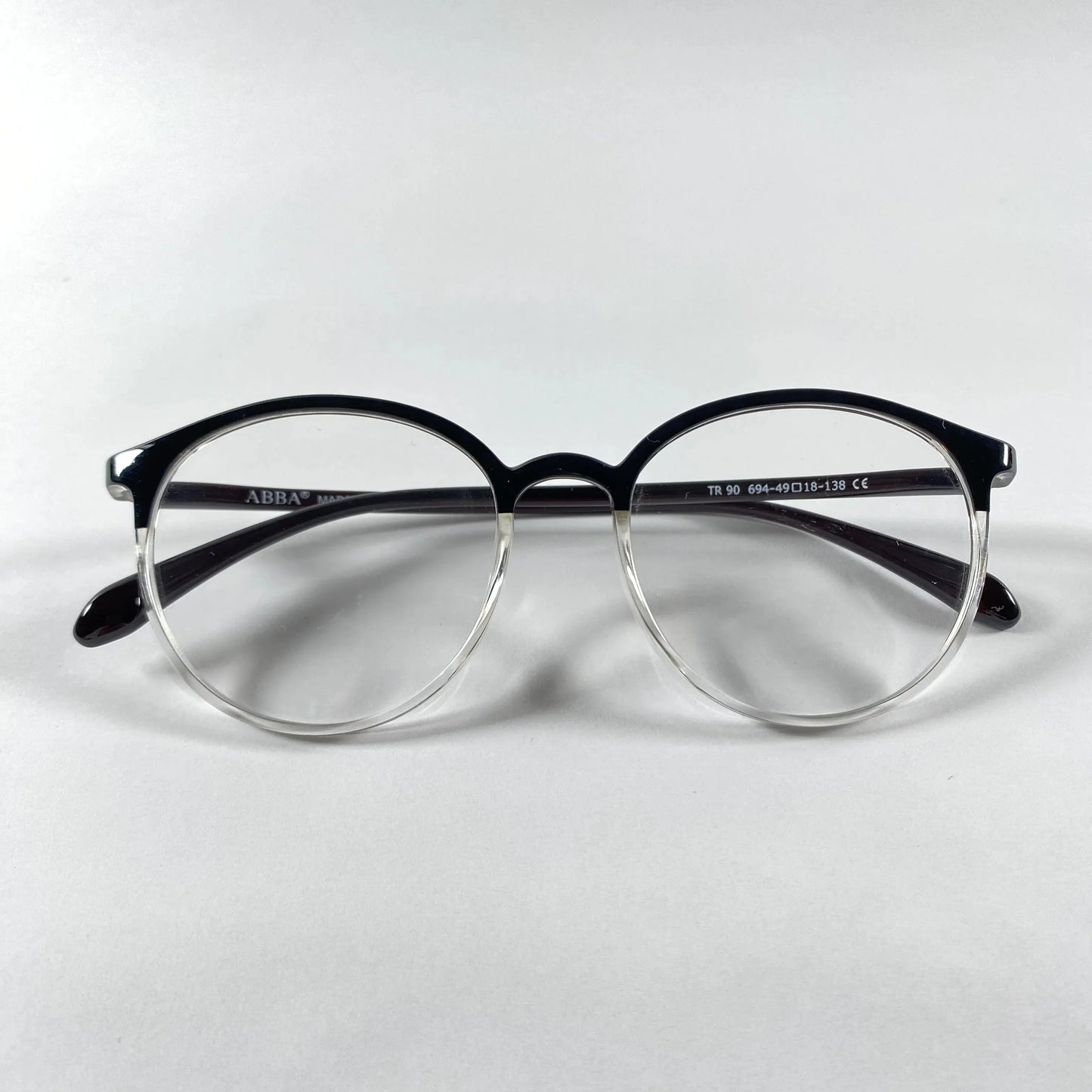 Round black clear plastic eyeglasses with transparent lower rims on white background