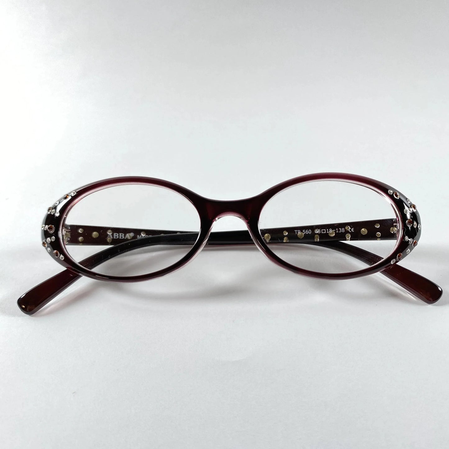 Oval burgundy glasses with crystal embellishments on the temples, product on white background