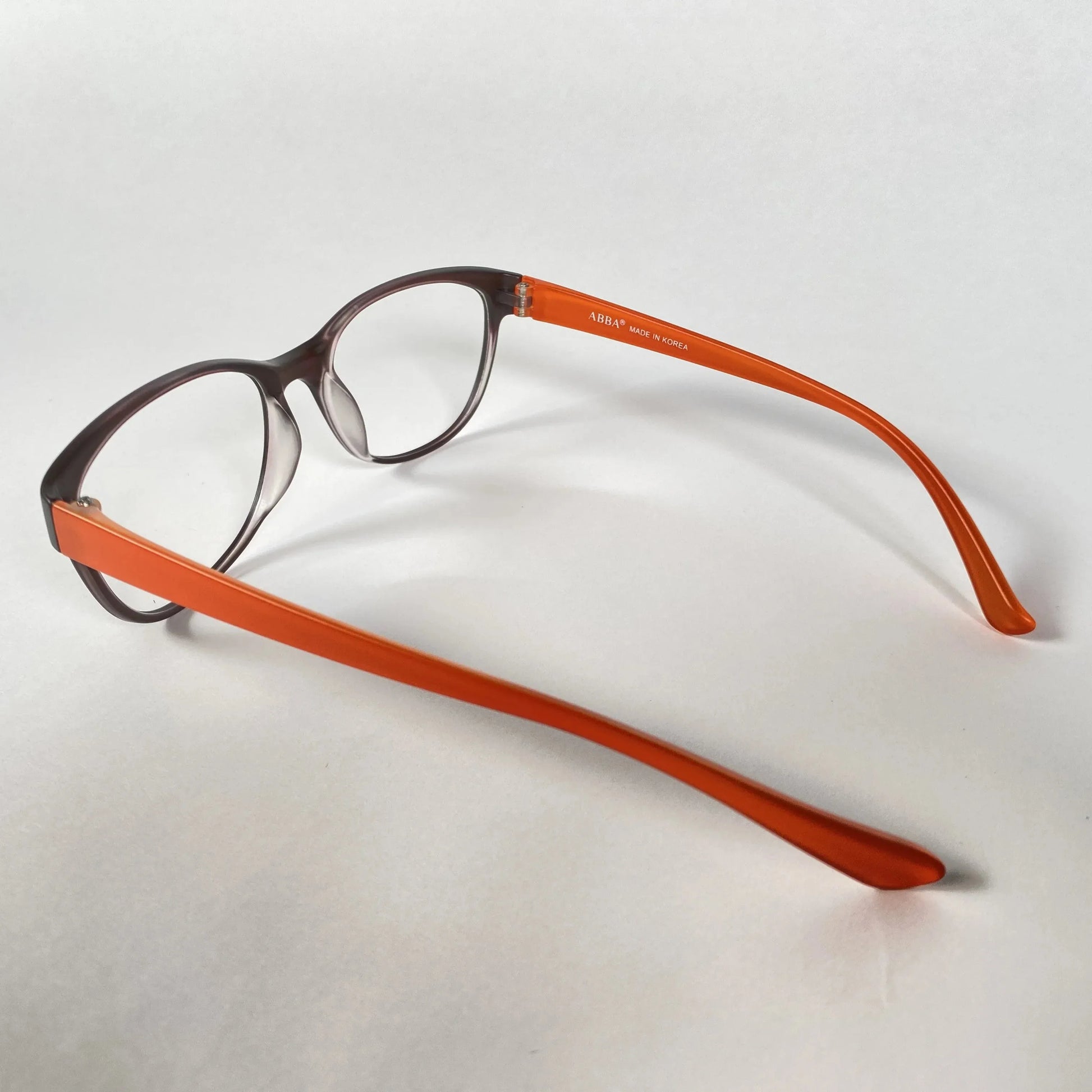 Brown and orange eyeglasses with clear lenses on a white background, side view.